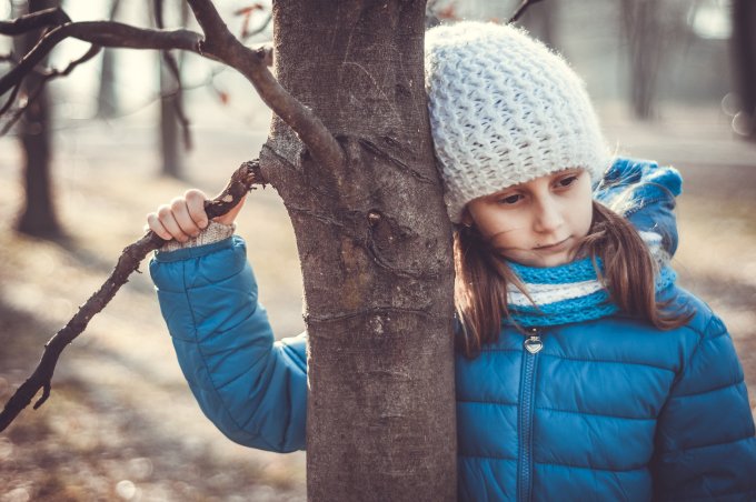 Kind lehnt sich an einen Baumstamm | © KHWE Ein junges Mädchen legt ihren Kopf sanft gegen den Stamm eines Baumes. | © KHWE