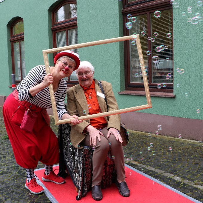 Clown unterhält eine Seniorin Ein Clown unterhält eine Seniorin im Rollstuhl. Im Hintergrund sind Seifenblasen zu sehen.