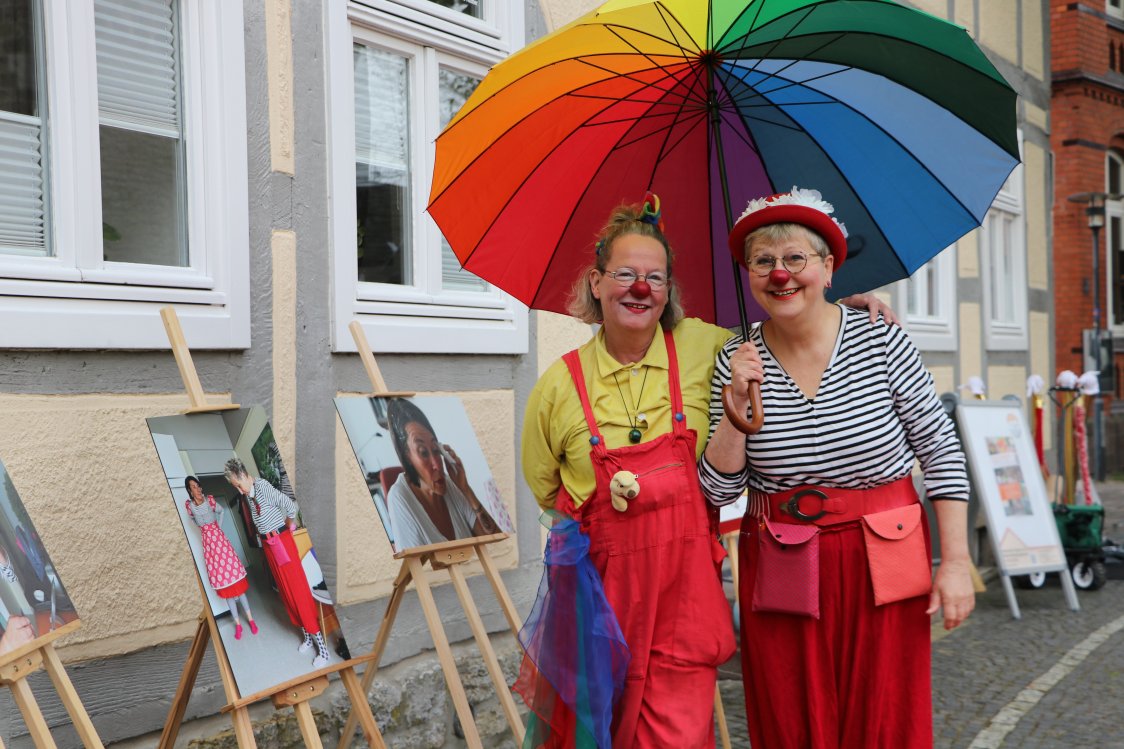 Zwei Mitarbeiterinnen, die farbenfroh als Clowns verkleidet sind und unter einem bunten Regenschirm stehen. | © KHWE